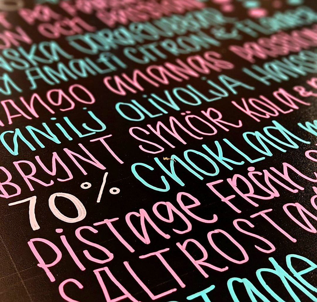 Close-up of pink and turquoise hand lettering on a dark board